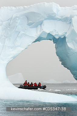 ANTARCTICA, TOURISM: Zodiac with tourists behind iceberg arch, Antarctic Peninsula