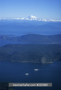 WASHINGTON, USA: Mt. Baker rises above San Juan Islands, Washington State Ferries crossing Puget Sound, aerial.