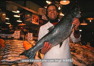 USA, WASHINGTON, SEATTLE: Pike Place Market,  salesman with salmon in front of open-air food display.